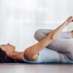 Mujer en postura del bebé feliz, abrazando sus pies con las manos, relajada en una esterilla de yoga.