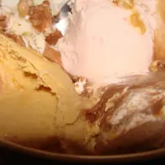 Un tazón lleno de helado de leche cremoso, con sabores de caramelo, fresa y chocolate, adornado con trozos de galleta.