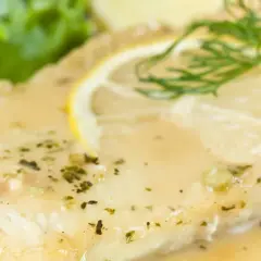 Filete de pescado bañado en una deliciosa salsa de limón para pescado, adornado con una rodaja de limón y eneldo.