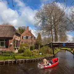 Paseo en barca por los canales de Giethoorn, Holanda, con casas de tejado de paja y un puente de madera.