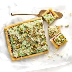 Ciasto z zieloną masą pistacjową i posiekanymi pistacjami, pokrojone na kwadraty.