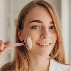 Uśmiechnięta kobieta z blond włosami trzyma różowy roller do twarzy. Zastanawiasz się, jaki roller wybrać? Ten model jest idealny do masażu.
