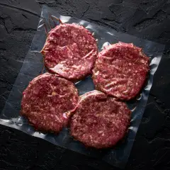 Cztery surowe kotlety na hamburgery w folii. Zastanawiasz się, mięso na hamburgery jak przyprawić?