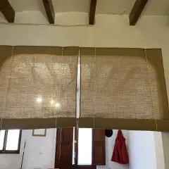 Dos estores enrollables caseros de tela rústica cubren una ventana y una puerta.