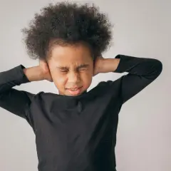 Niño con afro cubriéndose los oídos, mostrando malestar. Sugiere la necesidad de tratamiento para la ansiedad en niños de 5 a 12 años.