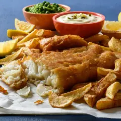 Un delicioso plato de fish and chips, con pescado rebozado crujiente, patatas fritas doradas, guisantes y salsa tártara.