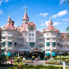 Grand hôtel rose de style victorien avec des tours, un grand cadran d'horloge et des jardins fleuris.