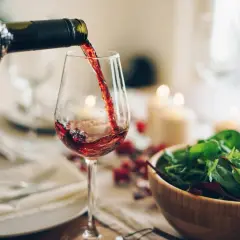 Versando vino rosso in un bicchiere, con un'insalata fresca e candele sullo sfondo. Un'atmosfera perfetta per gustare un buon greco di tufo vino.