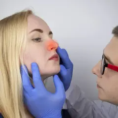 Médico examina la nariz de una mujer con enrojecimiento interno, sugiriendo pupas en la nariz por dentro.