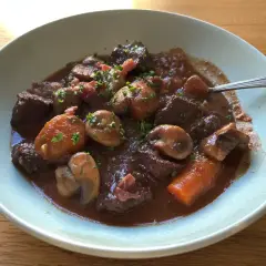 En mustig boeuf bourguignon med möra köttbitar, champinjoner och morötter i en djup rödvinssås, toppad med persilja.
