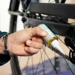 Dłoń z bransoletkami aplikuje olej na łańcuch roweru. To dbałość o detale, jak w centrumrowerowe zwroty.