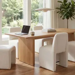 Modern dining room with a light wood table and plush cream chairs. A laptop and mug sit on the table, offering inspiration for how to choose dining chairs that blend comfort and style.