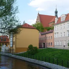 Nad rzeką malownicze kamienice. Chcesz wiedzieć, jak sprawdzić czy budynek jest w rejestrze zabytków? Spójrz na detale architektoniczne i wieżę kościelną.