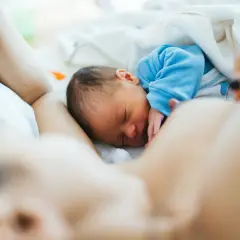 Malutki noworodek śpi wtulony w mamę. Jego brzuszek jest taki okrągły i słodki, jak u każdego niemowlaka.