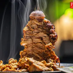 Gorący, parujący kebab z mięsa mielonego, obracający się na rożnie, z chrupiącymi kawałkami mięsa na talerzu.