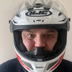 Hombre con casco de moto HJC blanco y rojo, listo para elegir su próxima aventura.