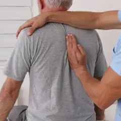 Fizjoterapeuta bada kręgosłup starszego mężczyzny.