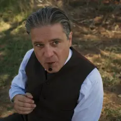 Un uomo con un sigaro in bocca, vestito elegantemente, sembra un re.