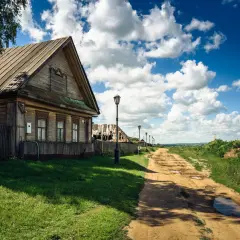 Drewniany dom i polna droga o minimalnej szerokości drogi, z latarniami i chmurami na niebie.