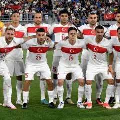 Piłkarze reprezentacji Polski i Turcji pozują do zdjęcia przed meczem. Białe stroje z czerwonym pasem i godłem.