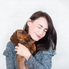 Un perro salchicha le lame la cara a su dueña, que sonríe con los ojos cerrados. Es la prueba de que mi perro me sigue a todas partes.