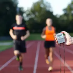 Trening interwałowy na bieżni. Dwie osoby biegną, a w dłoni trzymany jest stoper.