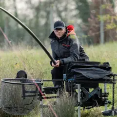 Wędkarz siedzi przy wodzie, trzymając wędkę. Delikatnie wygięta szczytówka sygnalizuje branie.