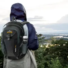 Osoba w kapturze z plecakiem gotowa na trekking górski, z widokiem na dolinę i rzekę.