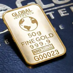 Sztabka złota 50g, czyli ok. 1.6 uncji, z napisem "FINE GOLD 999.9". Na tle ciemnej skóry z wytłoczonym globusem.