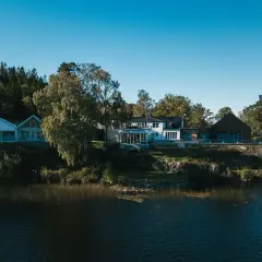Hällsnäs Hotell & Restaurang vid en sjö, omgivet av träd. En vacker plats för avkoppling och god mat.