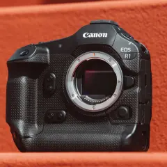 Profesjonalny aparat Canon EOS R1 z obiektywem na pomarańczowym tle.