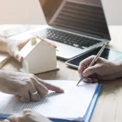 Podpisanie dokumentu, który może oznaczać odstąpienie od umowy najmu. Na stole model domu, laptop i tablet.