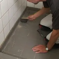 Man knäböjer och använder en borste för att ta bort silikonfog runt en dusch.