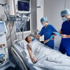 Médicos monitorean a paciente en UCI. Una enfermera ajusta el flequillo cortina de la joven mientras un doctor anota datos.