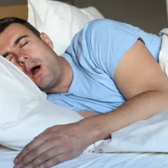 Uomo dorme a bocca aperta, spiegando perchè si sbava quando si dorme. La sua testa è appoggiata su un cuscino bianco.