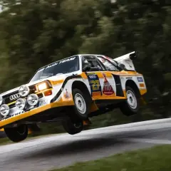 Klasyczny Audi Sport Quattro w akcji, unoszący się nad zakrętem. Ikona rajdów.