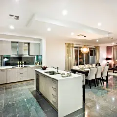 Cocina moderna con isla, comedor y sala de estar. Los focos cilindricos en el techo iluminan el espacio.