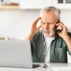 Zmartwiony mężczyzna rozmawia przez telefon, trzymając się za głowę. Może szuka siła wyższa powody problemów z laptopem.