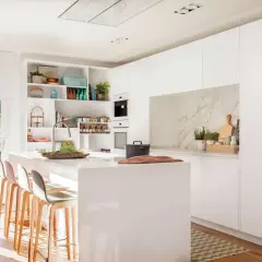 Elegante mueble cocina isla blanco con taburetes, encimera de cuarzo y vistas a un jardín con piscina.