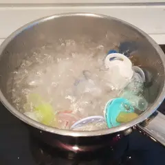 Flera färgglada nappar ligger i en kastrull med kokande vatten. Det är dags att koka nappar för hygien.