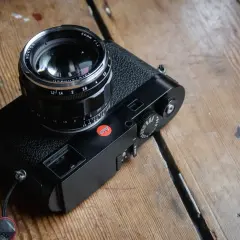 A black Leica M262 camera with a Nokton 50mm f/1.2 lens sits on a wooden surface.