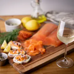 Un verre de vin blanc frais accompagne un saumon fumé et des toasts. Parfait pour savoir quel vin avec du saumon en papillote.