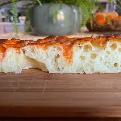 Fetta di focaccia soffice e alveolata, con pomodoro e formaggio filante. Perfetta per uno spuntino o un pasto veloce.