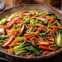 Pyszny makaron chiński z warzywami: grzybami shiitake, papryką, marchewką i pak choi, posypany szczypiorkiem i sezamem.