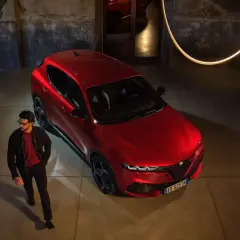 Elegancki mężczyzna obok czerwonego Alfa Romeo Tonale. Sprawdź aktualną alfa romeo tonale cena i odkryj jego styl.