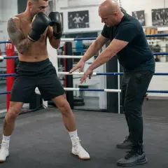 A boxing coach demonstrates proper footwork and all boxing stances to a fighter in a ring.