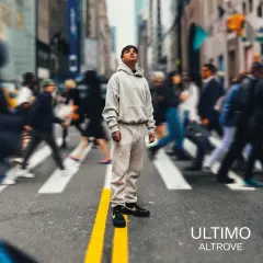 A young man in a grey tracksuit stands on a crosswalk in a busy city street, looking up.