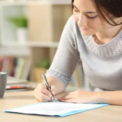Femme écrivant une lettre de motivation sur un bureau avec une tasse de café.