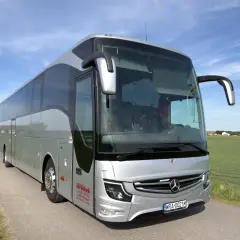Srebrny autokar na tle błękitnego nieba. Zastanawiasz się, ile miejsc ma autokar? Ten wygląda na przestronny, idealny na wycieczki.
