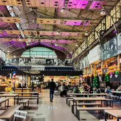 Wnętrze nowoczesnej vege restauracji w Warszawie. Widać stoły, ławki i stoiska z jedzeniem pod industrialnym dachem.